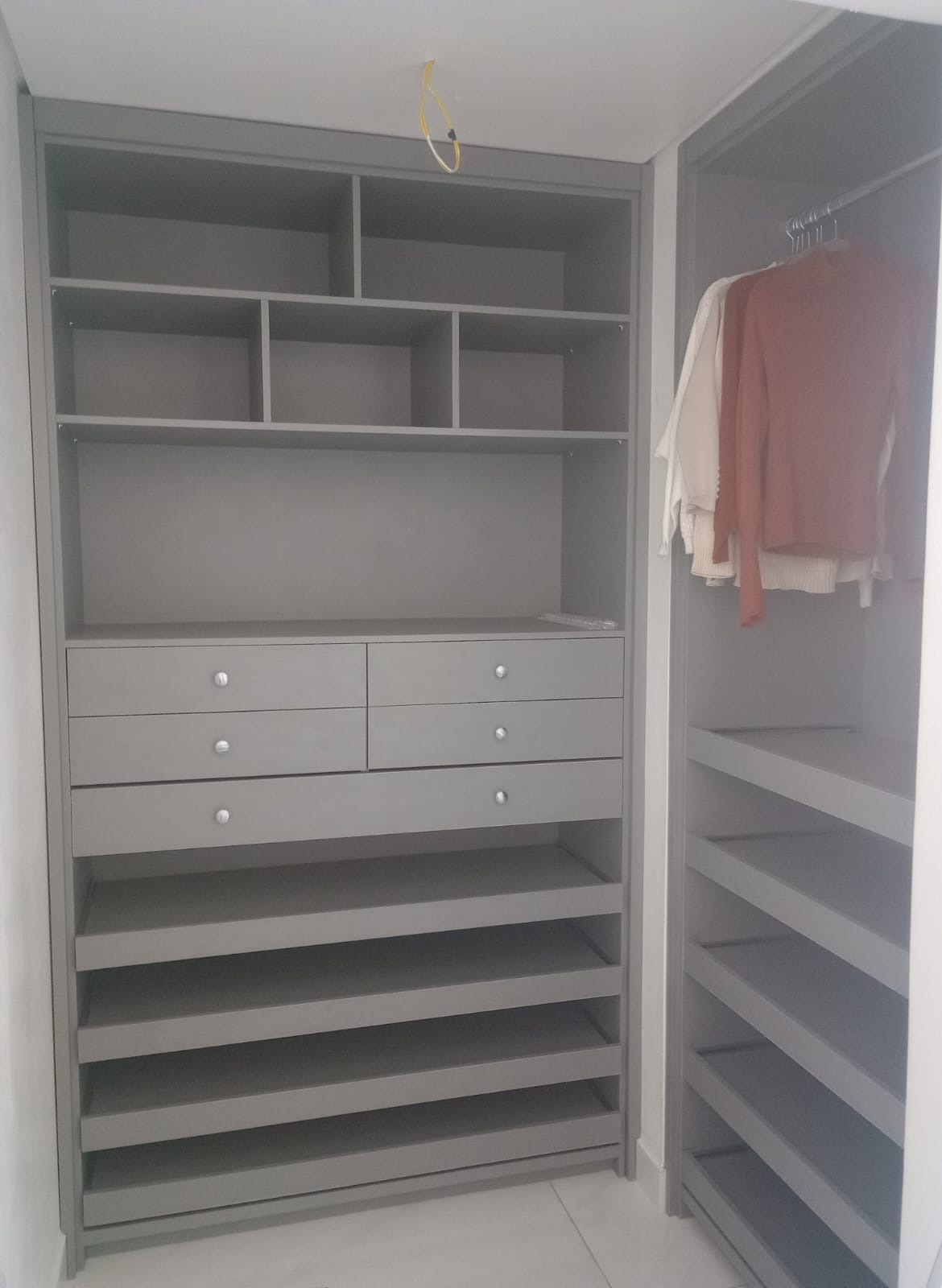 closet planejado cinza com prateleiras, gavetas com botões prateados e cabideiro com roupas penduradas