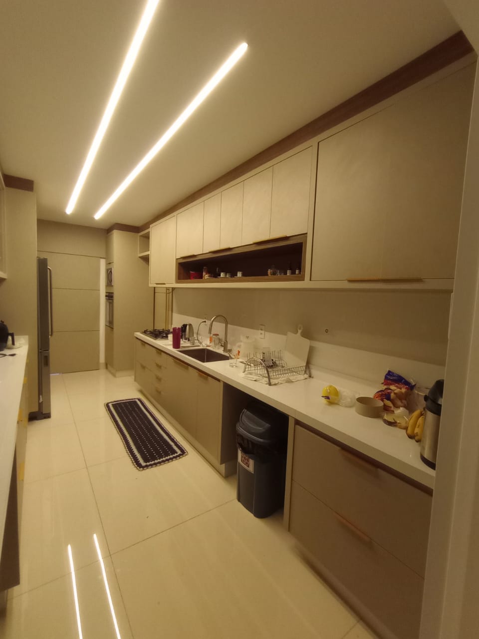 cozinha planejada beige com iluminação de LED embutida no teto, bancadas claras e armários