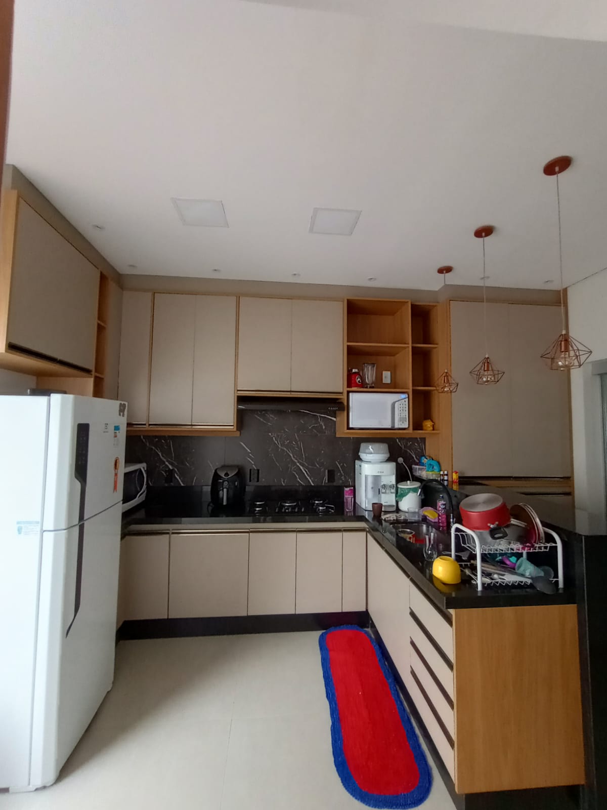 cozinha planejada com armários cinza e madeira, cooktop, micro-ondas e pendentes de cobre
